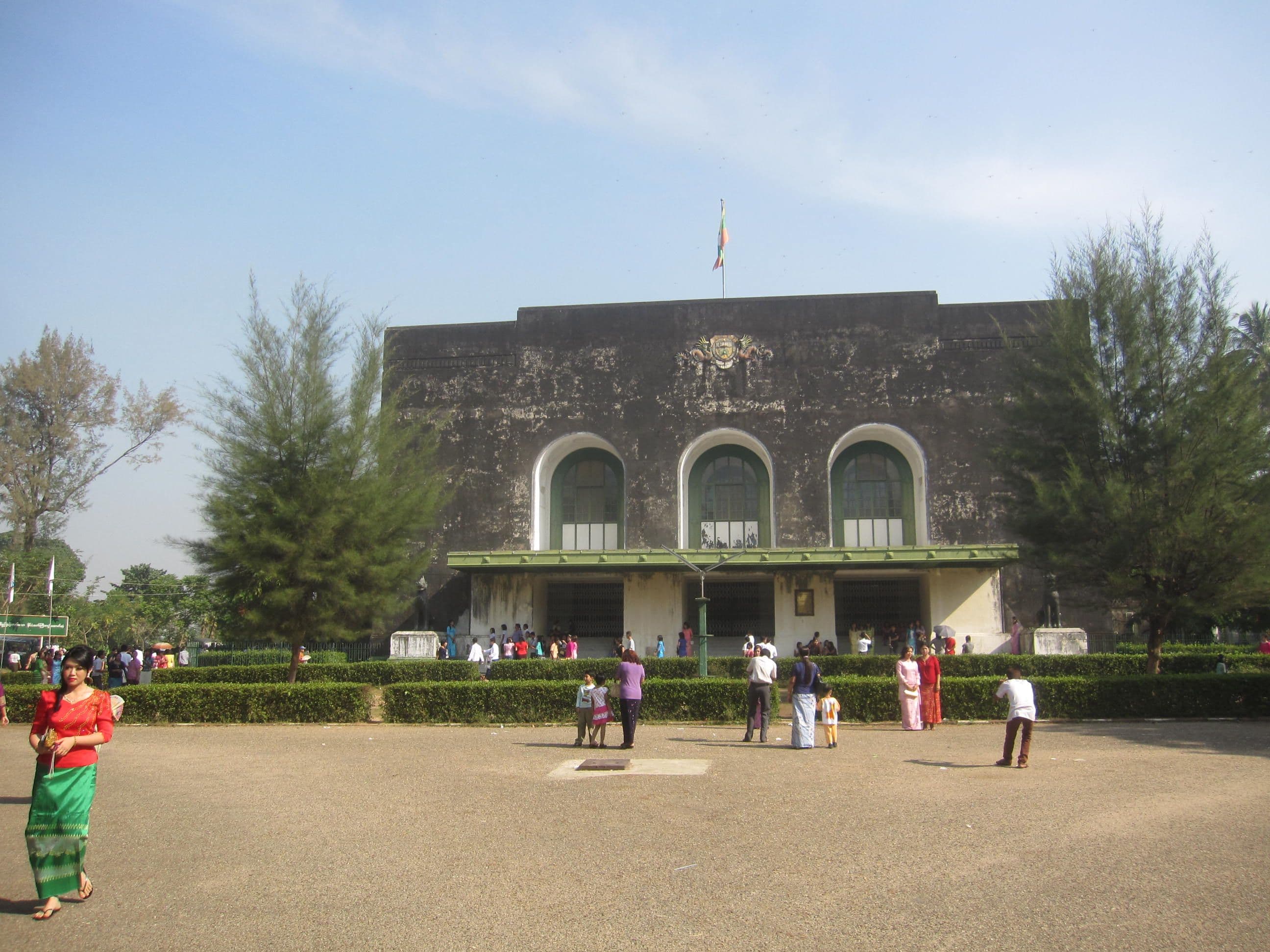 Dark stone building with three arched windows overlooks an open courtyard filled with people.