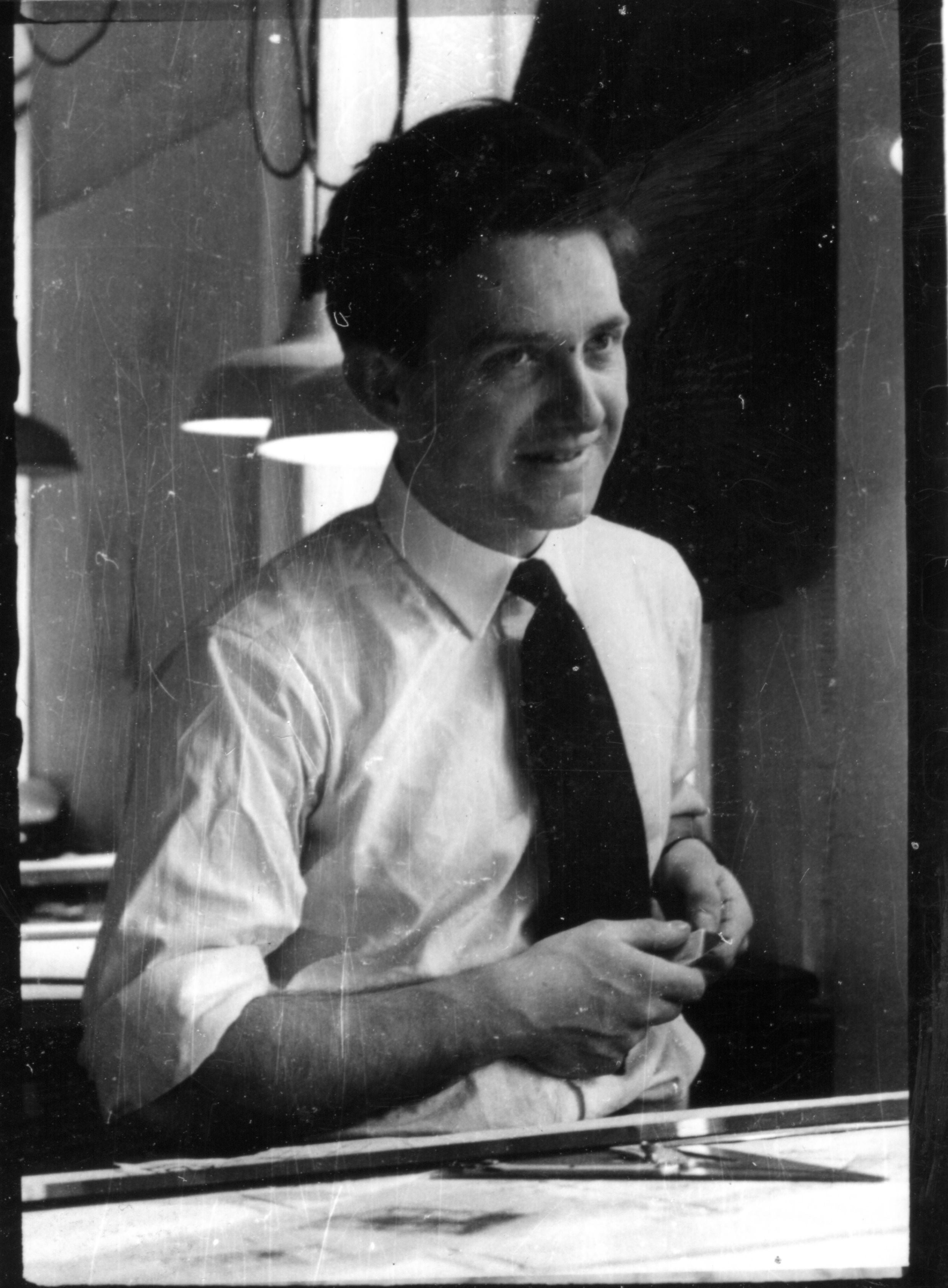 A smiling man in a collared shirt and tie poses behind a desk.