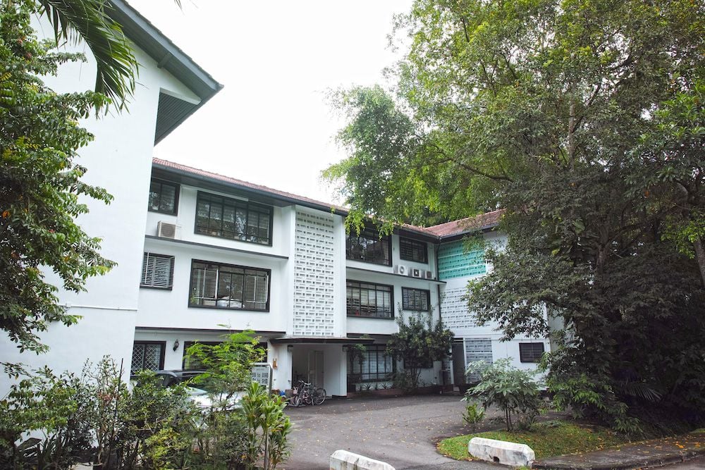 A white, multi-story building with many windows is surrounded by lush green trees.