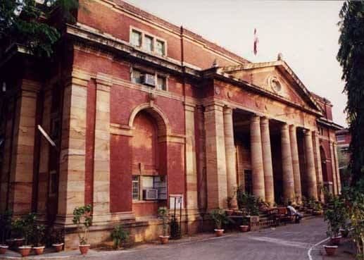 Historic red brick building with a grand stone portico and tall columns under a cloudy sky.
